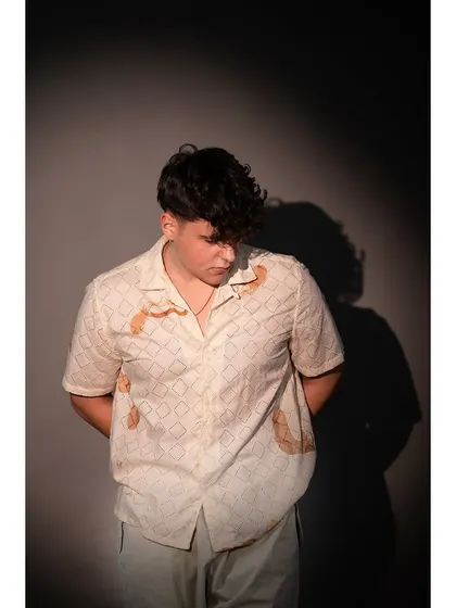 A close-up studio shot focusing on the details of a patterned shirt. The dramatic shadow and downward gaze create an introspective mood for a fashion editorial.