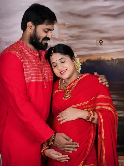 A beautiful, serene portrait of the couple in matching red traditional attire. The mom-to-be's peaceful expression captures the quiet joy of pregnancy.