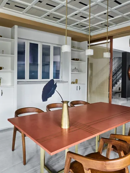 This dining room features a custom copper-topped table with brass legs, paired with classic wooden chairs. The coffered ceiling and built-in white cabinetry add a touch of timeless elegance.