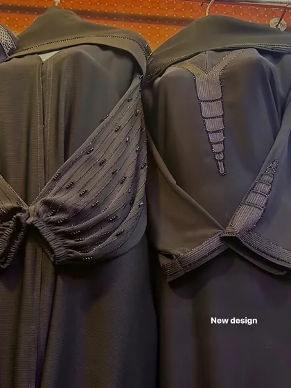 A close up of new abaya designs in a dark, charcoal grey. The details include intricate sleeve beading and textured fabric on the neckline and cuffs.