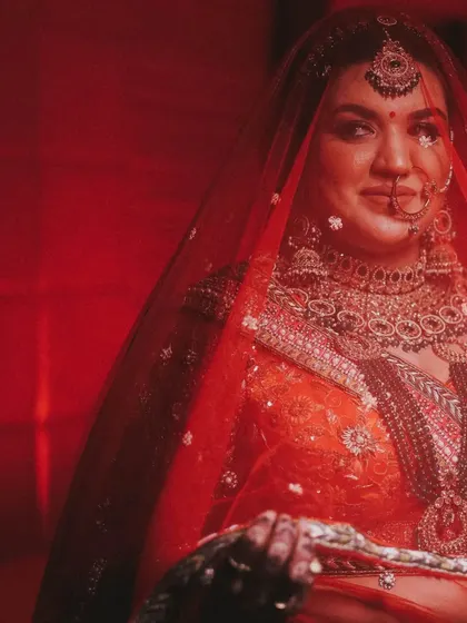 A striking bridal portrait with a bold red background, making the bride and her attire stand out.