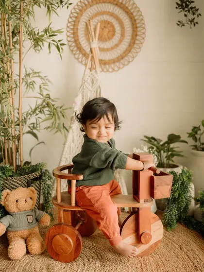 This little adventurer is ready to roll on his wooden tricycle, a favorite prop for toddler sessions.