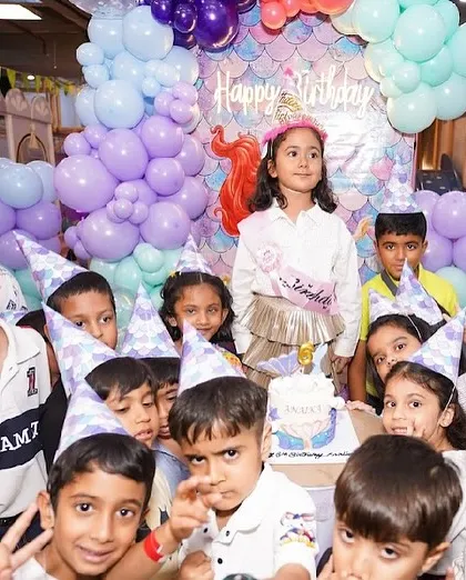 The birthday girl and all her friends, wearing party hats, gather for a group photo around the mermaid cake.