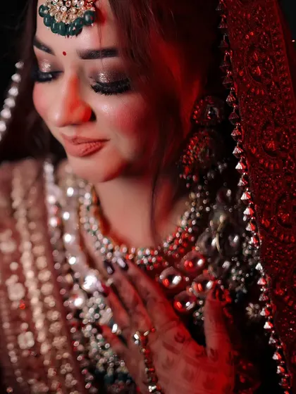 A close-up portrait capturing the bride's gentle expression. The soft red lighting adds a warm, romantic glow, drawing attention to her flawless makeup and beautiful jewelry.