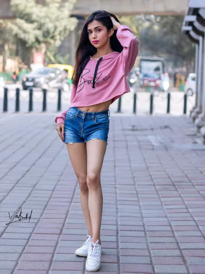 A full-length street style shot that captures the energy of the city. The model's pose is dynamic and confident, showcasing a trendy, casual outfit against a busy street backdrop.