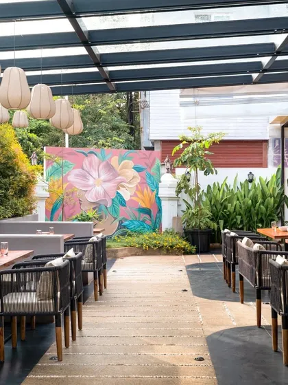 A full view of the Pink Verranda's outdoor dining area, showing how the seating arrangement, lush plants, and statement mural come together. The design creates a welcoming and visually rich atmosphere for guests.