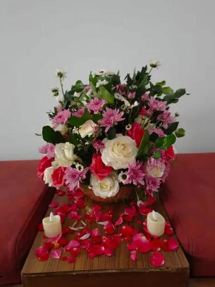 A lovely floral arrangement in a bowl, surrounded by scattered rose petals and candles, perfect for a side table or welcome area.