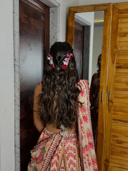 The back of her hair is styled with a beautiful waterfall braid and soft waves, adorned with fresh flowers.