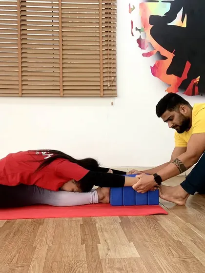 Using yoga blocks for support, I help a student ease into a deep Paschimottanasana (Seated Forward Bend), focusing on lengthening the spine.