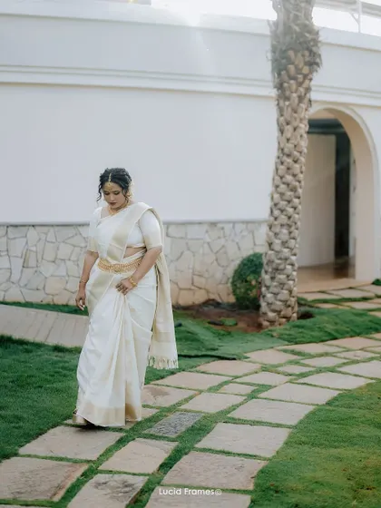A beautiful solo portrait of the bride in her elegant white and gold saree, walking through a garden.
