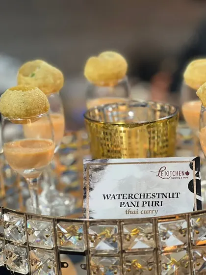 A creative fusion appetizer: Pani Puri shells filled with a waterchestnut and Thai curry mixture, served in elegant glasses.