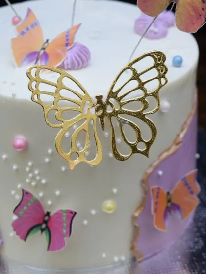 A detailed shot of the butterfly cake, focusing on the delicate gold acrylic butterfly and the colorful wafer paper butterflies that seem to flutter around the cake.