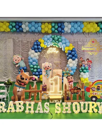A full-stage Cocomelon setup for a first birthday party, featuring a wide balloon garland, multiple character cutouts, and a custom backdrop.