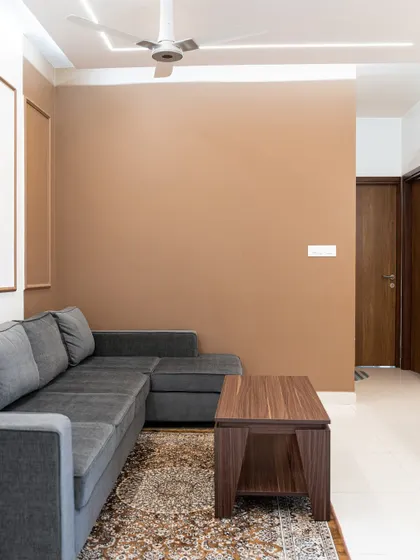 A simple yet stylish living space with an L-shaped grey sofa and a warm, earthy brown accent wall. This design shows how a minimalist approach can still feel cozy and complete.