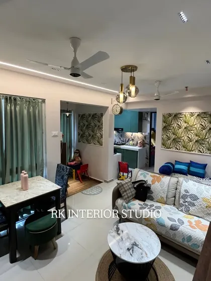 A wider angle of the living room, showing the compact dining table setup and the open flow into the kitchen. The use of matching wallpaper panels creates a sense of continuity in the design.