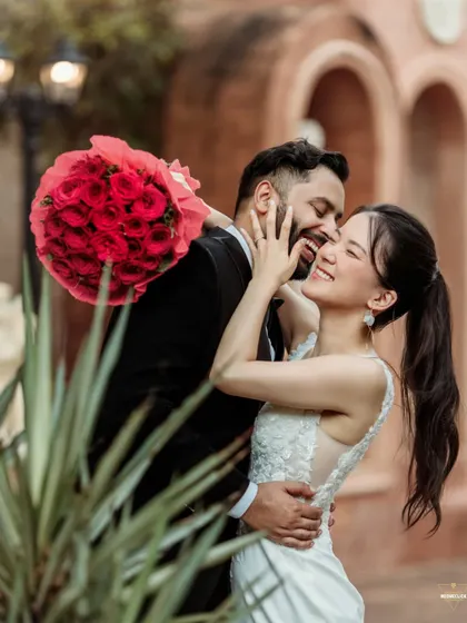 A moment of pure happiness and laughter. The bouquet of red roses adds a vibrant pop of color to this romantic, candid embrace. This photo shows that even in a formal shoot, we can capture spontaneous and joyful interactions.