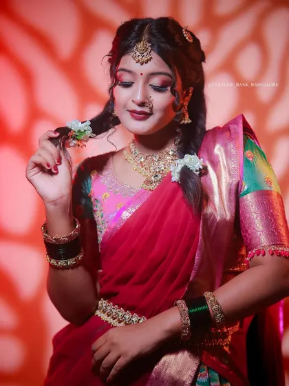 A model posing in a traditional red and green half-saree with braided hair, showcasing a complete festive look.