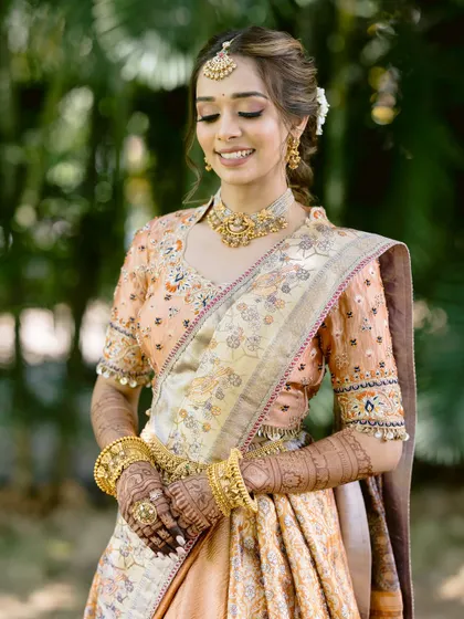 The bride looking down with a gentle smile. This shot highlights the intricate details of her saree, jewellery, and the flawless finish of her makeup.