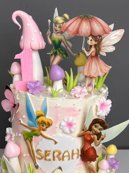 The top tier of our fairy house cake, featuring a large pink mushroom, the number '1' for a first birthday, and beautifully detailed fairy toppers, including one holding a tiny umbrella.