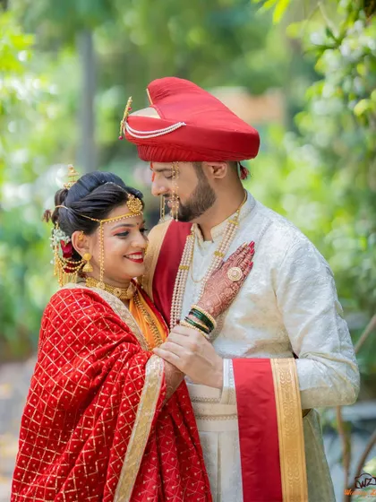 A close-up portrait of a Maharashtrian couple, highlighting the bride's intricate jewelry and the groom's traditional red pheta.