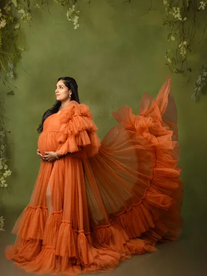 A graceful side profile of a mom-to-be, with the orange gown's train fanned out for a dramatic effect.