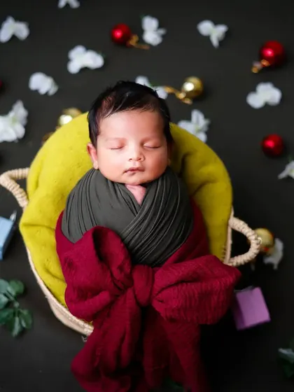 A festive setup with a baby wrapped like a gift in a basket, surrounded by holiday ornaments.