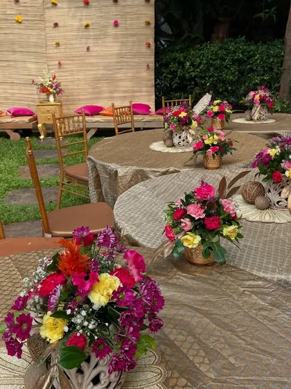 The guest seating at an outdoor Mehandi function. The tables are decorated with colorful floral centerpieces, and the low seating on the side provides a traditional touch.