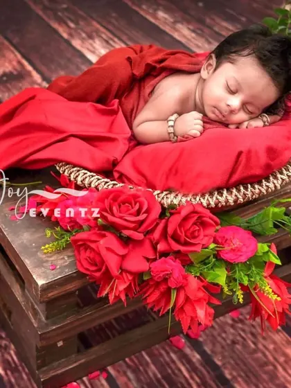A bold and beautiful newborn photoshoot with a rustic theme. The baby is draped in rich red fabric, resting on a wooden crate adorned with vibrant red roses, creating a striking color contrast.