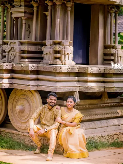 A classic portrait of a couple in matching golden-yellow outfits, seated by a stone chariot. This shot is a perfect blend of tradition and romance.