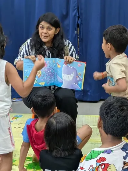 An instructor captivates the children with an illustrated storybook. You can see the excitement and curiosity on their faces as they interact with the story, shouting out answers and acting out the scenes.