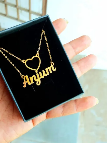 This minimalist name necklace features a single name alongside a simple, open-heart charm. It's a delicate and understated piece, perfect for everyday wear and shown here in its gift box.