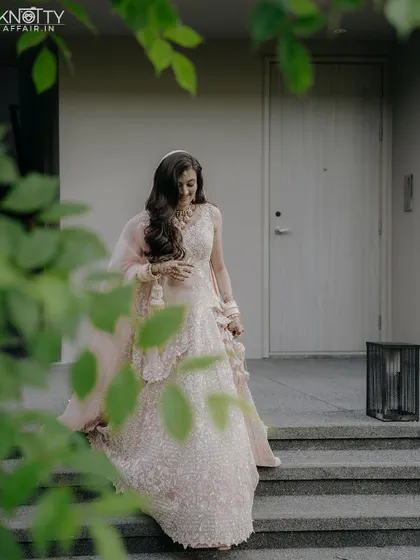 A beautiful portrait of the bride in her pastel pink lehenga, framed by lush green leaves. This shot captures her serene beauty just before she walks down the aisle at her Thailand wedding.