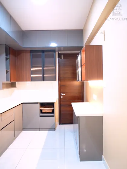 This L-shaped kitchen combines glossy grey laminate cabinets with wood-finish accents for a touch of warmth. The design includes open shelving for wicker baskets, providing a practical and stylish storage solution for vegetables or other essentials.