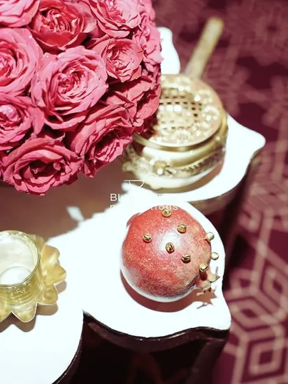 An overhead shot of a small table, showing a perfect sphere of pink roses and a pomegranate studded with cloves, a fragrant and traditional detail.