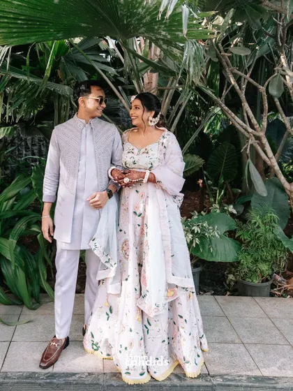 A classic couple portrait from the Haldi ceremony, set against a lush green backdrop that makes their pastel outfits pop.