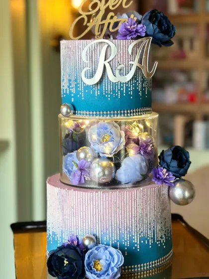 Love baked in hues of blue and purple. This dreamy three-tier cake features a sparkling drip effect and a clear center tier filled with beautiful flowers, perfect for a modern couple.
