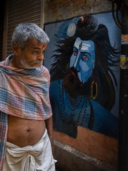 A man in Varanasi glances towards a mural of Lord Shiva, creating a visual parallel between the devotee and the deity.