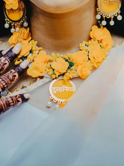 A close-up of the bride's floral jewelry for the Haldi ceremony, with the word 'Dulhania' (Bride) on her necklace. It's a beautiful detail that adds a personal touch to the celebration.