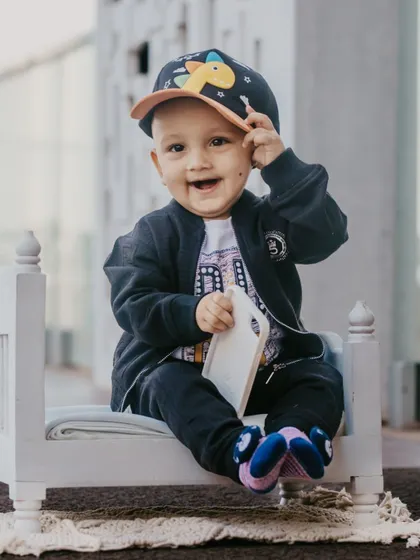A cool little guy with a cap and a big smile, posing on a miniature bed for his urban-themed pre-birthday shoot.