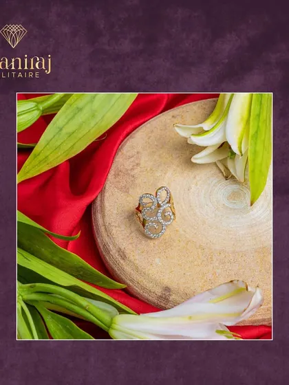 Elegance in every curve. This swirling diamond ring is set on a wooden block, surrounded by fresh lilies, highlighting its organic and artistic design.
