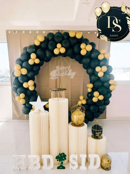 A simple yet bold black and yellow balloon wreath. This setup is perfect for creating a focal point in any room, with clean white plinths and marquee letters ready for the cake and celebration.