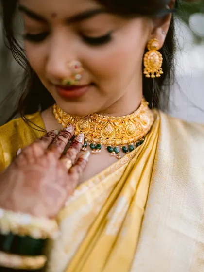 A close-up detail shot of the bride's traditional gold choker and her mehendi-adorned hand.