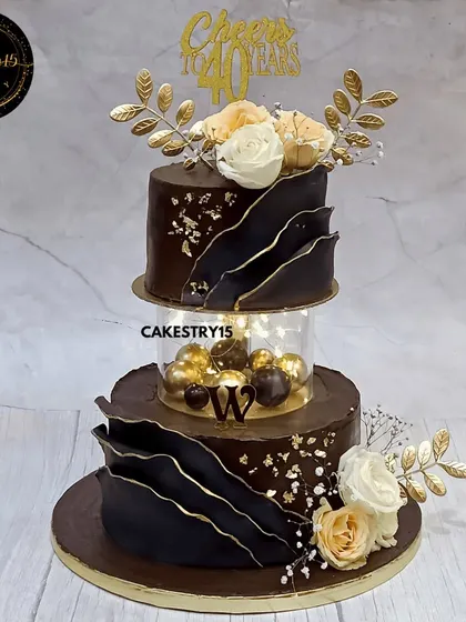 Celebrating a 40th birthday calls for something truly special. This two-tier chocolate cake features a modern, luxurious design with bold chocolate sails, an illuminated spacer, and elegant floral toppers, creating a sophisticated centerpiece for a milestone event.