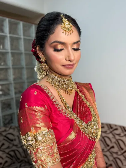 A classic South Indian bridal look with a red and gold silk saree, featuring golden eyeshadow and traditional jewelry.