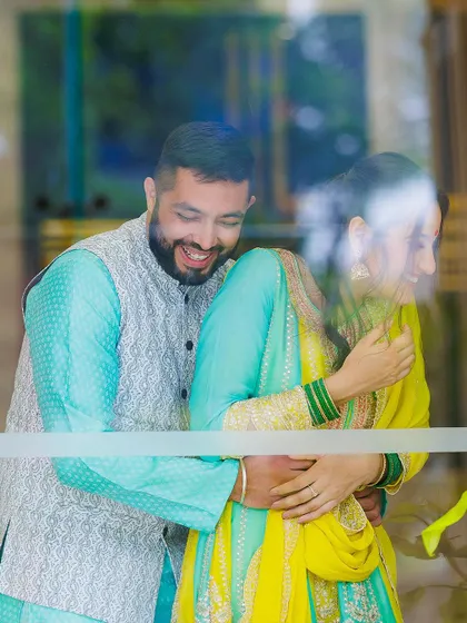 The pure joy of a candid moment. This photo, taken through a window, captures genuine laughter and a playful embrace during a Roka ceremony, showing our non-intrusive approach.