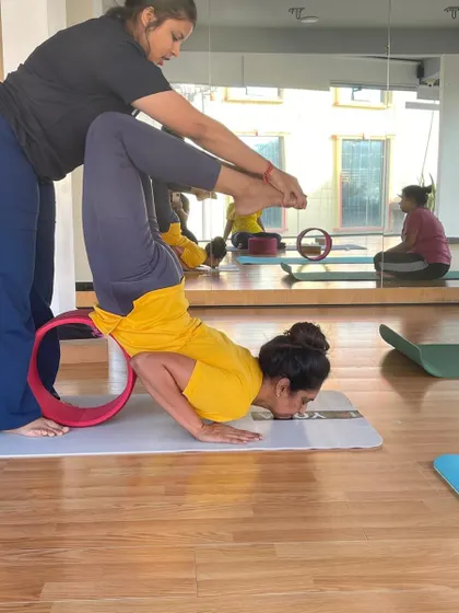 An instructor helps a student into an advanced arm balance on the wheel, showcasing our commitment to helping students progress.