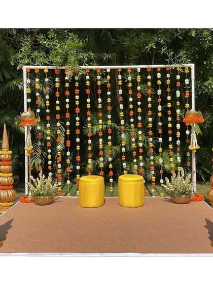 A clean and modern Haldi backdrop with marigold strings and traditional golden props.