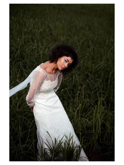 A close-up from the editorial bridal series, focusing on the bride's expression and the delicate, pearl-studded sleeves of her gown. This shot has a dreamy, ethereal quality.