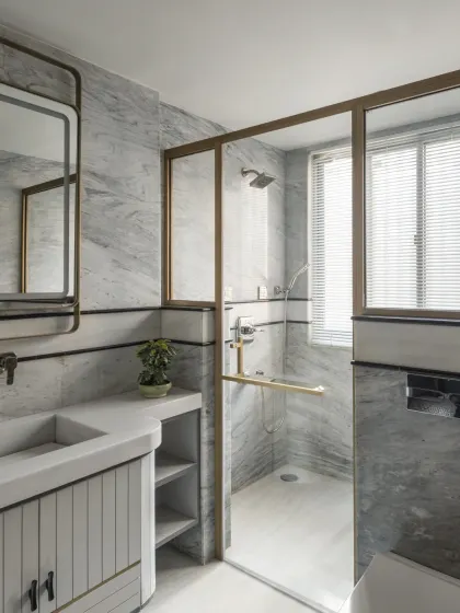 This bathroom in the Slender House uses grey marble-textured tiles and a clean, white vanity to create a bright and spacious feel. The glass shower partition and large window ensure the compact space is filled with natural light.