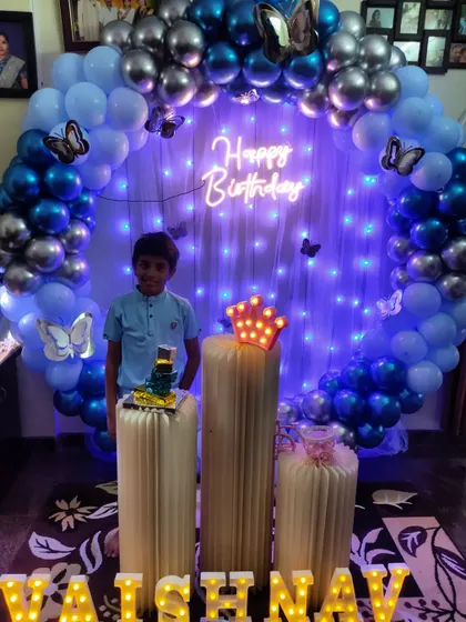 A happy client enjoying his blue and silver butterfly-themed birthday setup. The cool blue lighting gives the entire decoration a unique and vibrant glow.